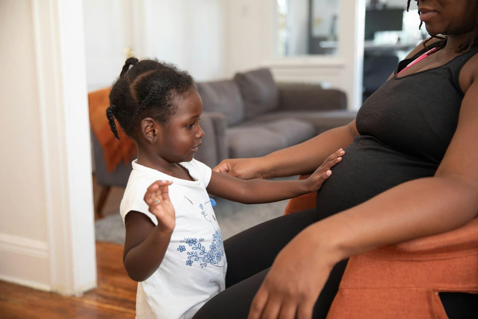At home, a small girl reaches out to touch her mother's pregnant bump.