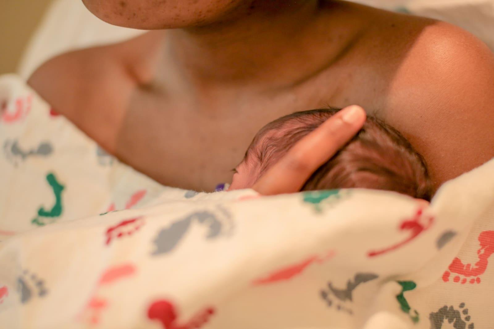 A newborn rests skin to skin on a mother's chest, her hand cradling the baby's head.