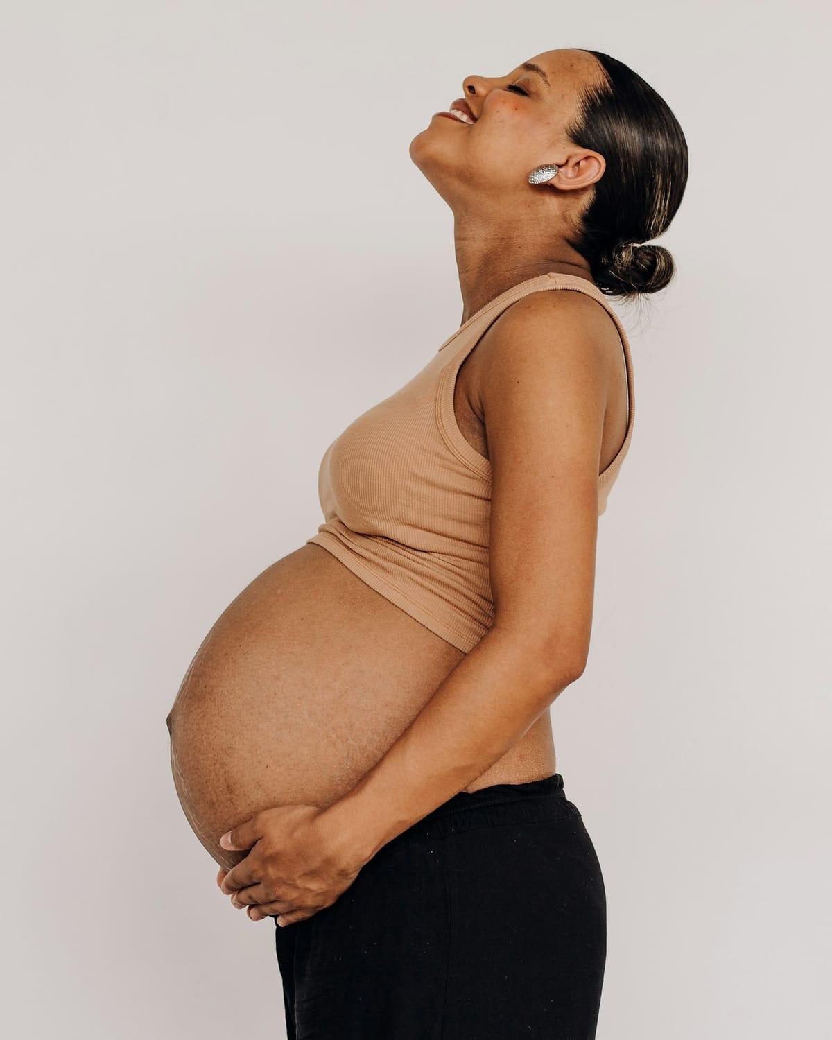 A pregnant woman in profile, holding her bump, her face turned up and smiling.