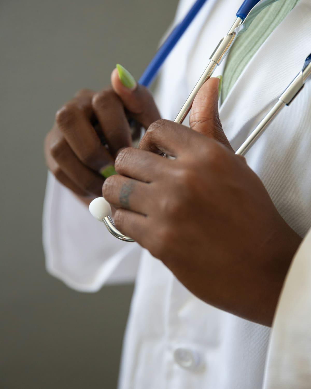 A clinician in a white coat holds a stethoscope in both hands.