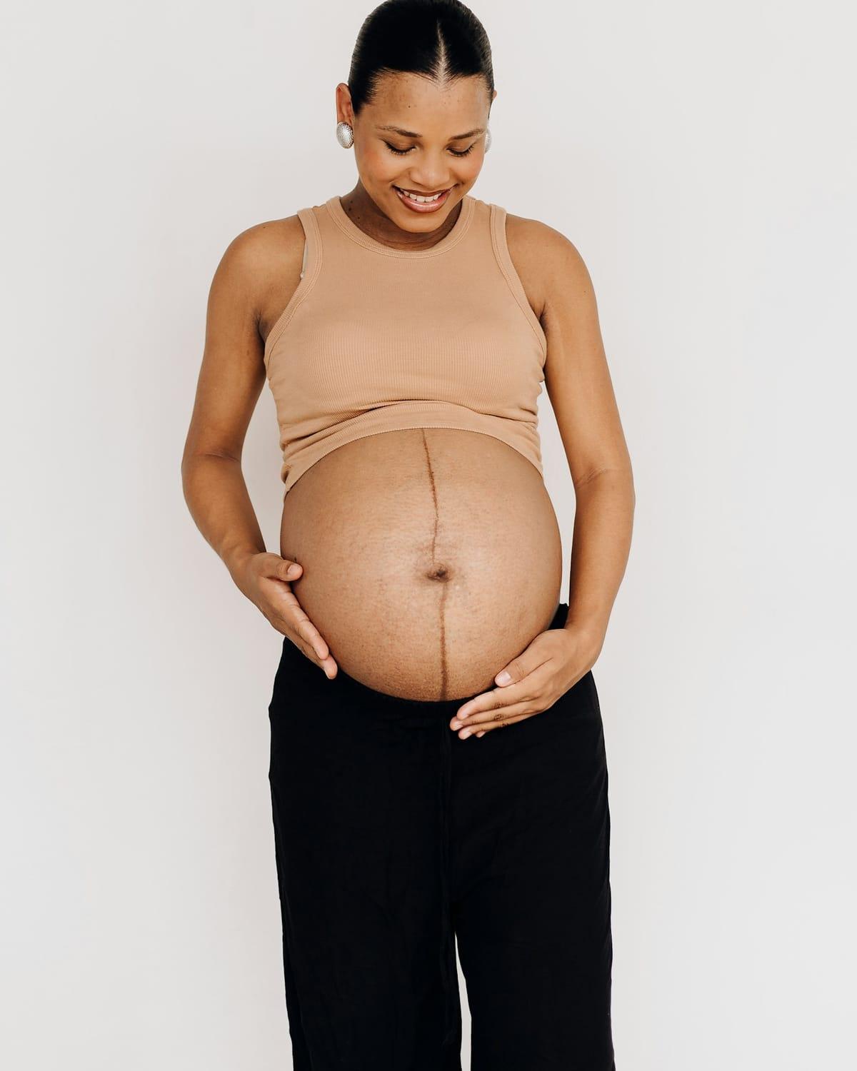 A pregnant woman smiles down at her bump, her hands resting on it.